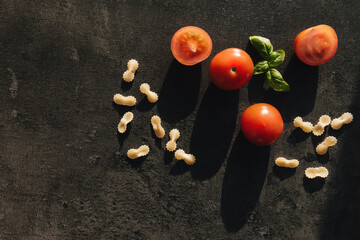 Fototapeta na wymiar Red cherry tomatoes, green basil, butterfly vermicelli pasta on gray background