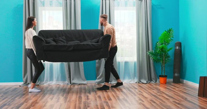 A happy young couple is bringing a couch to their new home. They sit down and enjoy buying their own apartment. They are smiling and happy because their biggest dream has come true. Tey are looking at