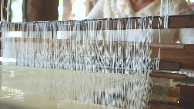 Asian old woman weaves silk fabric on a hand-held antique loom. Authentic handmade silk textile from silkworm cocoons. Traditional Silk Production In Thailand.