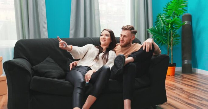 Couple planning out furniture before they unpack. Dreamy young family couple first time home buyers owners relax on sofa dreaming planning happy future goals in new own home flat