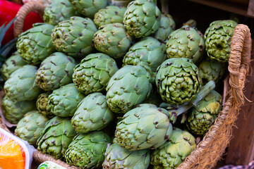 Fototapeta na wymiar Pile of fresh young buds of artichokes on showcase of greengrocery