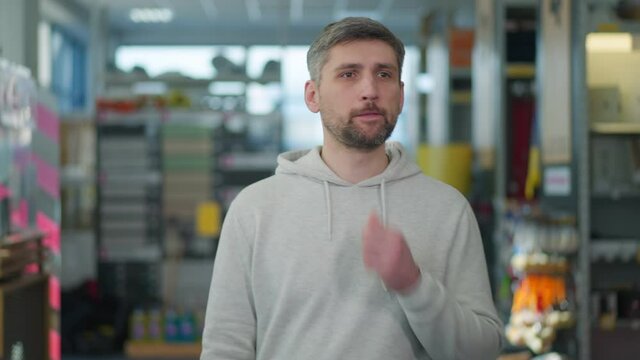 Portrait of thoughtful Caucasian handsome man looking around at rows of goods in hardware store, and leaving. Positive confident male buyer choosing tools or supplies in shop indoors.