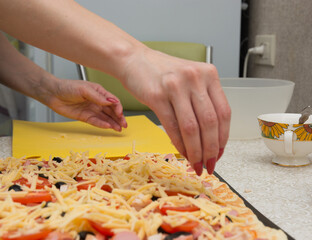 woman sprinkles pizza with grated cheese. homemade pizza cooking concept.