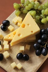 maasdamer cheese. Piece of cheese maasdam or maasdamer,green and black grapes  on wooden board on brown background.Hard cheeses. Dairy products.Healthy and tasty snack.Switzerland maasdam cheese