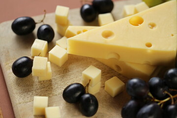 maasdamer cheese. Piece of cheese maasdam or maasdamer,green and black grapes brush on wooden board. Hard cheeses. Dairy products.Healthy and tasty snack.Switzerland maasdam cheese