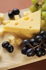 maasdamer cheese. Piece of cheese maasdam or maasdamer,green and black grapes brush on  board on brown background.Hard cheeses. Dairy products.Healthy and tasty snack.Switzerland maasdam cheese