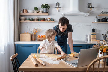 Cute preschool boy and his father baking cookies for International space Day using video lesson on...