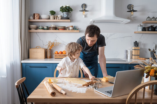 Cute Preschool Boy And His Father Baking Cookies For International Space Day Using Video Lesson On Laptop