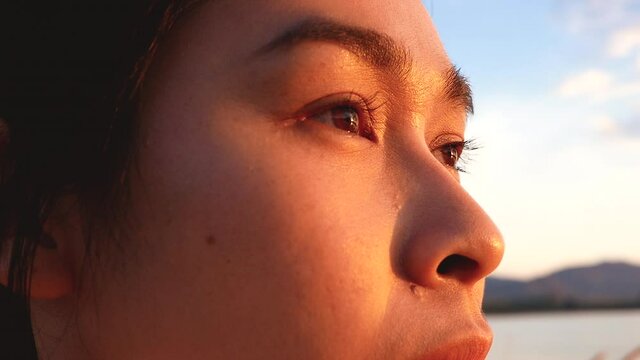 Close up shot of the side face of  hopeful woman looking away to nature reflection on water at sunset lakeside.