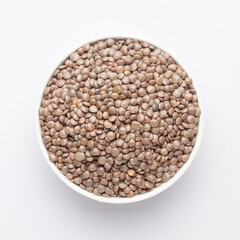Close up of Organic masoor dal (Lens culinaris) or whole brown  dal on a ceramic white bowl. Top view 