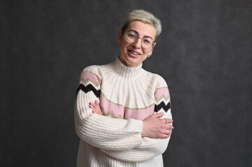 Adult Caucasian blond woman with short haircut stands straight with smile on gray background