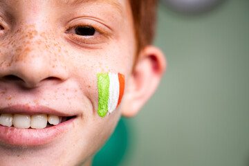 Close up of smiling kid with saint patricks day tricolour Irish flag on kids face during festival celebration wih copy space