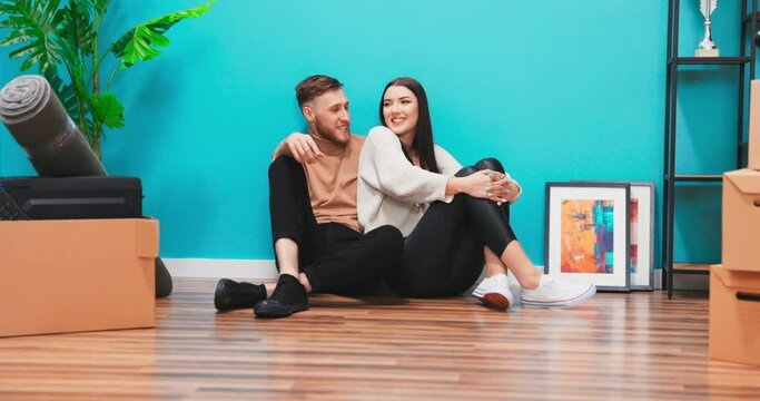 Close up of young couple in new apartment. Man and woman sitting on the floor among boxes planning interior design. They are very happy. They look at the camera and smile at the end.