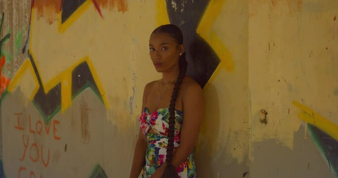 A young woman with sexy eyes stands at a wall with gafitti art in an abandoned building