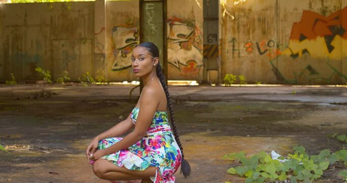 Sexy young girl in a long flower dress turns while squating at an abandoned warehouse on the Caribbean island of Trinidad