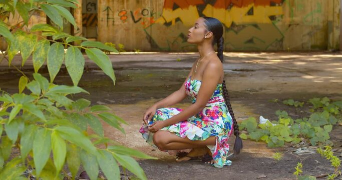 A sexy young woman squats at an abandoned warehouse with grafitti art in the background
