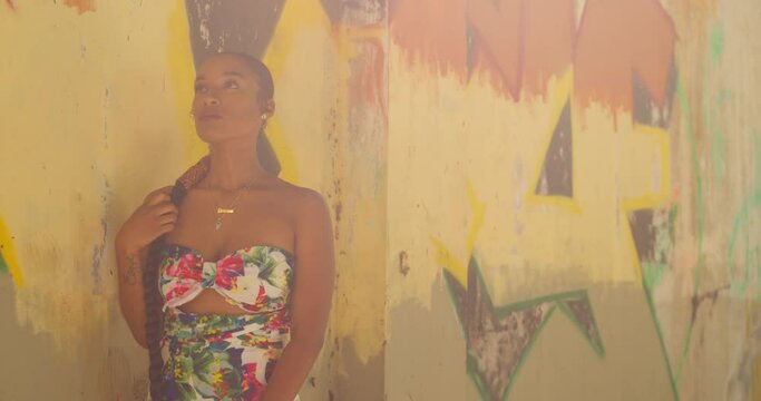Sexy girl in a flower dress plays in her while standing next to grafitti on a wall