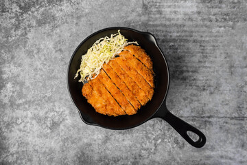 Tonkatsu or Japanese pork cutlet on black mini pan with sliced cabbage.