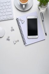 White office desk with mock up mobile phone, coffee cup, notebook and copy space on white background.