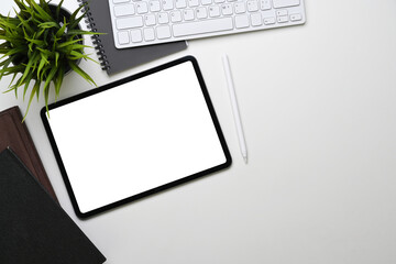 Top view of white office desk with digital tablet, keyboard, notebook and plant.