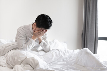 Young man sitting in bed hiding his face in hands 