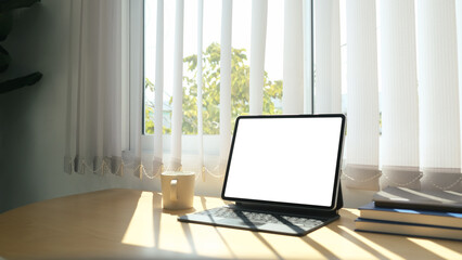 Close up view of computer tablet, coffee cup and books beside the window with sun light shine through the curtain.