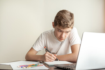 Onlay is a drawing lesson. A teenage boy draws a pencil in an album, in front of him are pencils and a laptop stands.