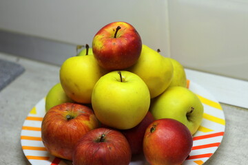 A heap of apples in a plate on the table. Red and green juicy ripe apples lie in a slide on a white plate against the background of a gray wall. Stock photography fruit top view