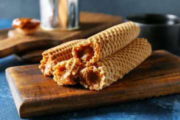 Tasty wafer rolls with boiled condensed milk on color background