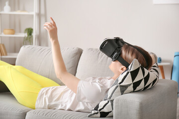 Young woman with virtual reality glasses lying on sofa at home