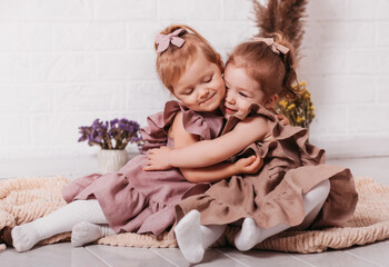 Two little girls cuddle in a pigtail on the floor and laugh