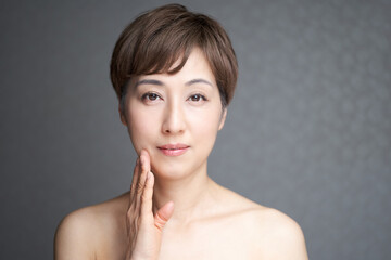 Obraz na płótnie Canvas 口角を押さえてカメラ目線で微笑む中年の日本人女性