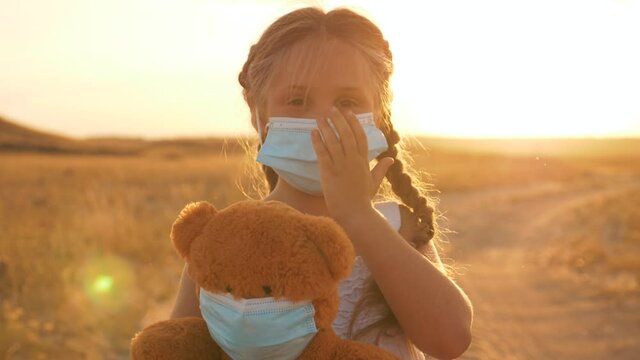 A child stands on the field with a soft toy in his hands. A child in a medical mask isolated during the quarantine of the virus. A kid plays doctor with a Teddy bear. The concept of health care.