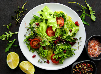 Fresh green mixed  salad bowl with tomatoes and microgreens  on black concrete background. Healthy food, top view.
