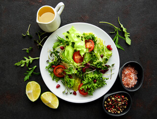 Fresh green mixed  salad bowl with tomatoes and microgreens  on black concrete background. Healthy food, top view.