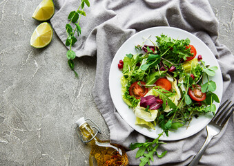 Fresh green mixed  salad bowl with tomatoes and microgreens  on  concrete background. Healthy food,...