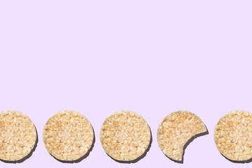 Whole and bitten round gluten-free rice loaf on purple background copy space