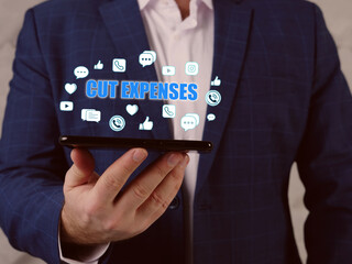 Fototapeta premium CUT EXPENSES text in search line. Businessman looking at smartphone. Cost cutting&nbsp;refers to measures implemented by a company to&nbsp;reduce&nbsp;its&nbsp;expenses&nbsp;and improve profitability