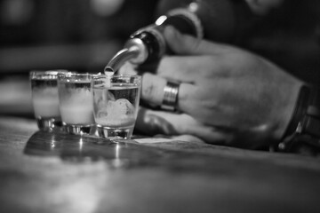 Black and white image of bartender filling shots at the counter