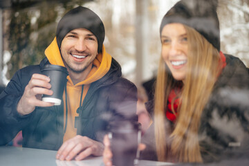 Young loving couple drinking coffee in a cafe behind the glass