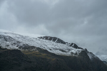 Minimalist gloomy highlands landscape with snow-capped high mountains in overcast weather....