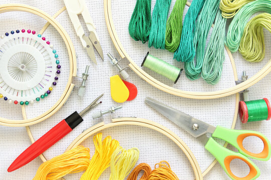 Embroidery hoop and multicolored accessories on white linen canvas with spools of thread, needle and scissors.