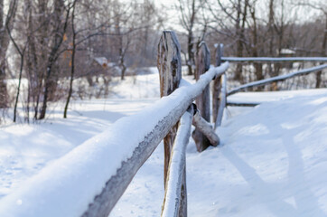 Snow-covered wooden fence made of long poles.