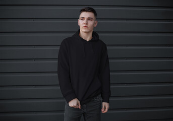 Mockup of a black men's sweatshirt with a pocket on a guy on a metal wall background, front view.