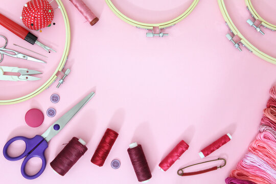 Composition with sewing accessories on a pink background with needles, a spool of thread, scissors and a measuring tape