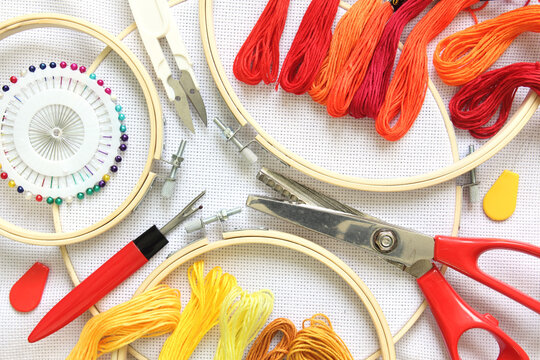 Embroidery hoop on white fabric canvas close-up with sewing accessory, scissors, embroidery threads and needle.