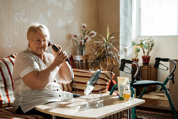 Senior beauty and skincare. Senior elderly plus size blonde woman with Disability styling hair near mirror at home.