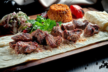 Appetizing beef kebab with grilled vegetables, bulgur and pickled onions on a wooden board
