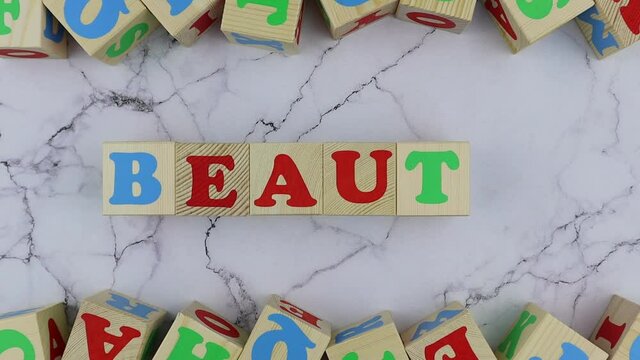 Beauty concept with colorful alphabet letters on wooden cubes centered between top and bottom borders of additional alphabet blocks on a marble background. Stop motion, top view