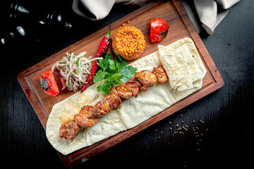 Chicken kebab cooked on the grill with lavash, bulgur and grilled vegetables on a wooden board....